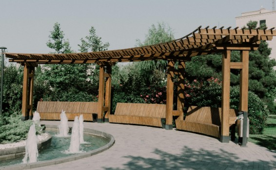 Pérgola de gran luz con bancos integrados Pérgola de madera curva de gran luz con bancos integrados en una zona ajardinada